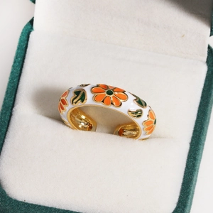 Macro view of floral enamel pattern with white and orange petals on a gold open ring