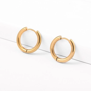 Detailed view of polished gold hoop earrings with clicker closure on white display