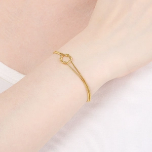 Close-up of a double-layered gold snake chain bracelet with a central knot on a wrist