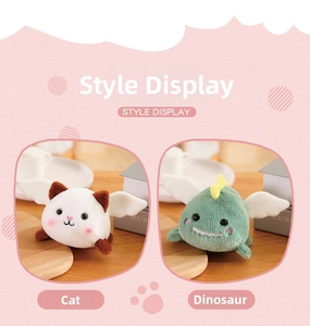 Detail view of plush cat and dinosaur doll pendants with small white wings on a wooden surface