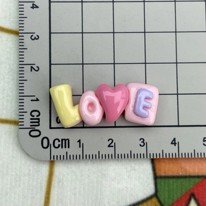 Macro shot showing 3.5cm pink resin LOVE heart charm on a ruler for size reference