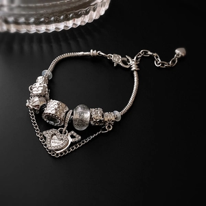 Detail of silver snake chain bracelet with heart charm and spread wings engraving