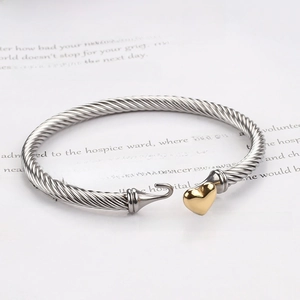 Close-up of twisted silver steel cable bracelet with a golden heart charm and hook closure