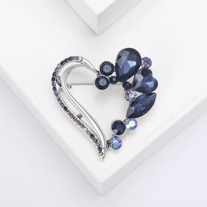 Macro detail of silver heart brooch with gradient blue and purple crystals on white stand