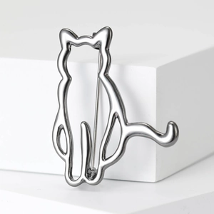 Macro shot of silver cat silhouette brooch on white geometric prop with metallic shine