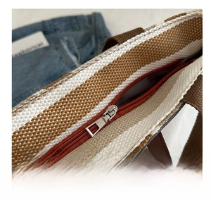 Detail of smooth metal zipper and striped canvas texture on the top of the tote bag