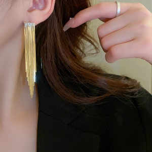 Close-up of elegant gold long tassel earrings with tiered metal chains on female model