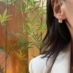 Detail of gold pearl earring worn by model with a natural bamboo and wood background