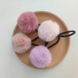 Close-up of four fluffy faux rabbit fur pom pom hair ties in pink and purple shades