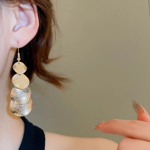 Detail of gold layered disc tassel earrings featuring textured irregular metal surfaces