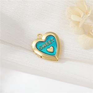 Detail view of a gold heart locket with teal enamel and Sweet engraving on fabric