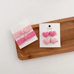 Detail of pink bow and heart hair clips on a white card inside a wooden tray