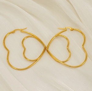 Détail des boucles d'oreilles doubles cœurs dorés sur un tissu en satin blanc
