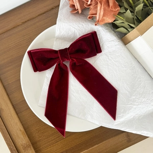 Detail of dark red velvet bow hair clip showing luxurious texture on white porcelain