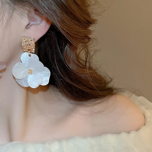 Detail shot of large white acrylic flower earrings with gold textured square studs on model