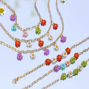 Close-up of gold chain necklaces with colorful floral beads on a reflective surface