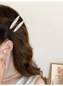 Détail de barrettes à motif marbre avec strass colorés sur cheveux bruns et ondulés