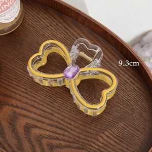 Detail view of a 9.3cm acrylic heart bow hair claw clip with a purple gemstone inlay