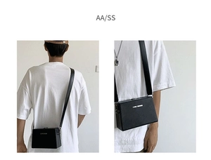 Detail of black box crossbody bag with wide shoulder strap and white logo lettering