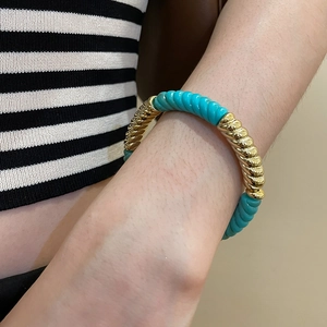 Detailed close-up of a gold and turquoise acrylic twisted geometric bracelet on a wrist