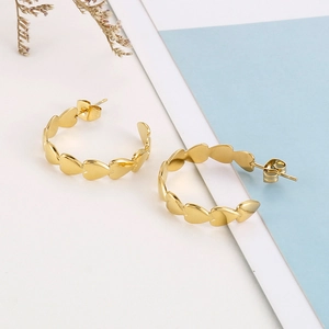 Macro shot of gold-plated titanium heart-shaped hoop earrings on a minimalist background