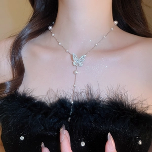 Dettaglio del ciondolo a farfalla in zircone e collana di perle su pelle glitterata