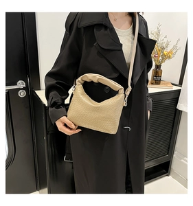 Detail of beige crocodile pattern handbag with pleated strap on black coat