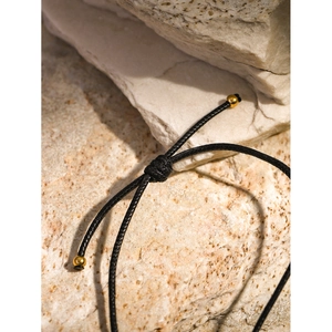 Detail of adjustable black wax cord with gold sliding beads on a textured stone surface