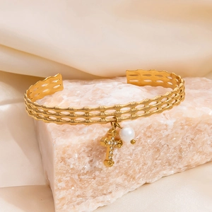 Detailed close-up of golden hollow cuff bracelet with cross pendant and pearl on crystal