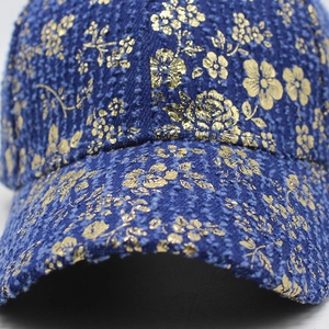 Detail of blue denim baseball cap featuring elegant gold floral patterns and rich texture