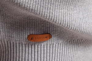 Detailed close-up of light grey knit fabric with a brown leather logo tag and fine texture