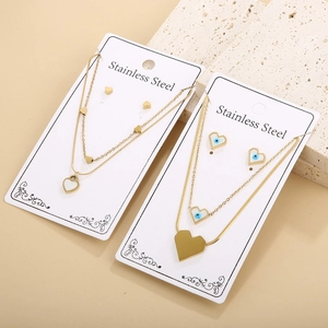 Detailed view of two gold stainless steel jewelry sets with heart and evil eye charms