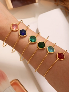 Macro shot of stacking thin gold bangles featuring six colorful faceted square stones