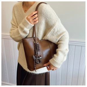 Detail of a dark brown leather tote with white stitching and cute creative charms