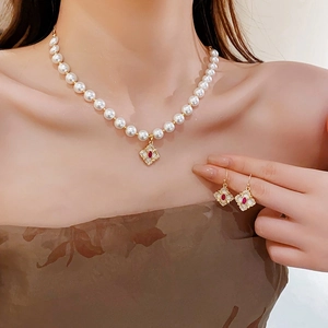 Gold plated floral pearl necklace and earrings set with red gems and clover motifs