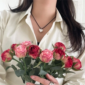 Detail of 925 sterling silver heart necklace worn by a model with a bouquet of pink roses