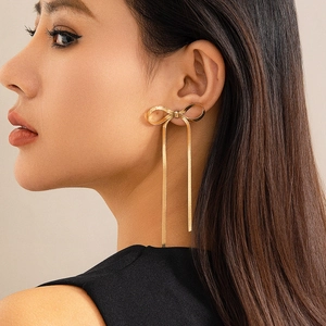Golden bow earrings with long snake chain tassels on a model in soft lighting