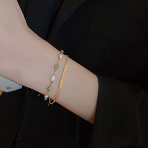 Close-up of stacked gold plated bracelets with green and white beads on a model's wrist