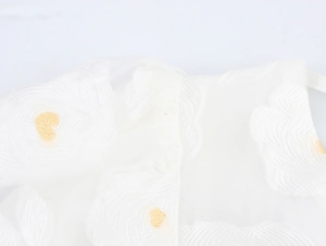 Detailed macro view of white tulle fabric with delicate floral embroidery and gold accents