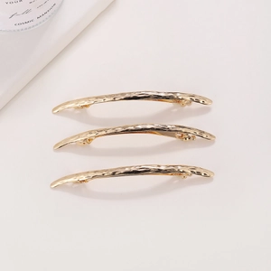 Close-up of three gold metal hair clips with hammered texture and arc spring design