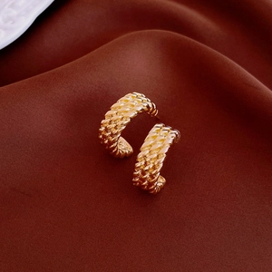 Close-up of golden metallic C-shaped earrings with fine woven texture on silk fabric