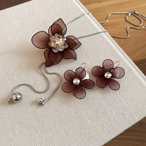 Detail of mesh flower necklace and earrings set with crystal centers on fabric background