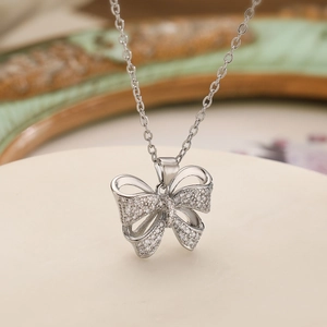 Elegant silver bow pendant necklace with sparkling cubic zirconia on a round display pedestal