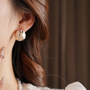 Detailed view of cream and gold spiral swirl stud earring on ear with silver needle