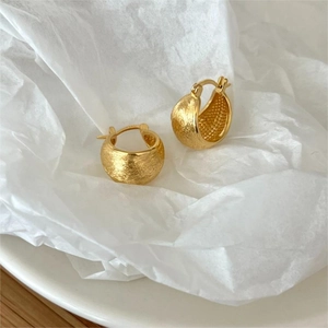 Detail shot of golden brushed texture hoop earrings on white pleated paper background