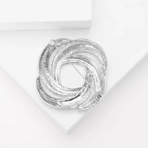 Minimalist silver geometric swirl brooch with textured finish on white blocks