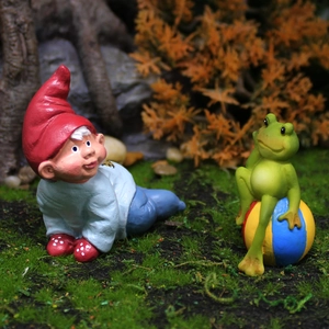 Garden gnome with red hat and blue clothes with green frog on a striped ball ornament