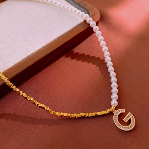 Détail macro du collier en perles et chaîne dorée avec pendentif G serti de zircons