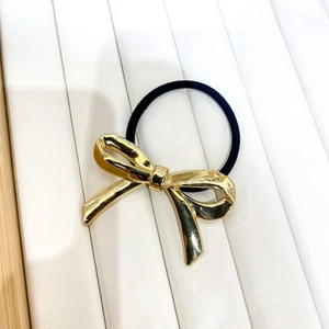 Detail of a golden metal bow hair tie with a black elastic band on a white texture base