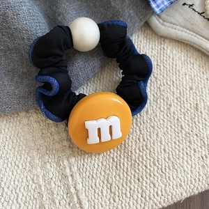 Gros plan sur chouchou en tissu noir avec bord bleu, perle et breloque jaune lettre M